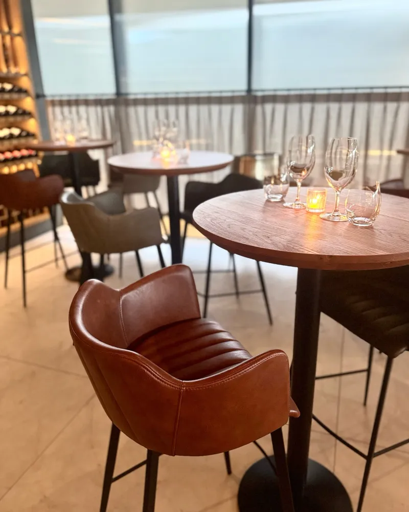Tan leather tub chairs and candlelit tables beside the window at 81 Bay wine bar
