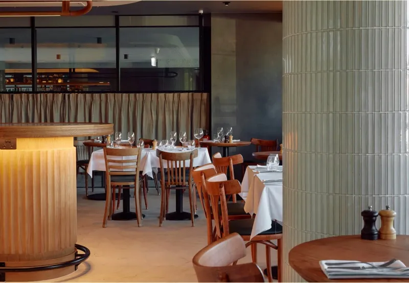 White linen tables and timber chairs at 81 Bay wine bar with green tiled columns