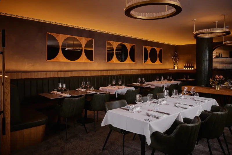 Baix dining room with white linen tables, green leather chairs and arc wall panels