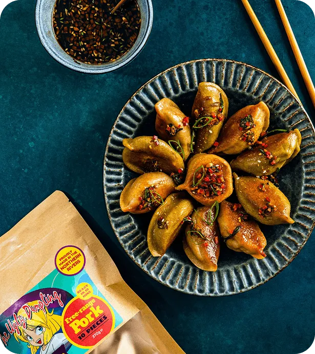 Plate of glazed free-range pork dumplings topped with fresh chilli beside a bowl of sesame dipping sauce