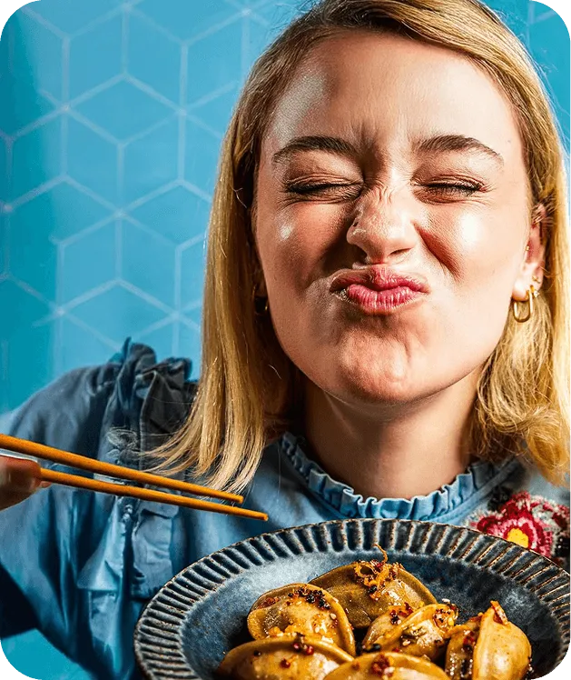 A delighted customer scrunching her face over a plate of dumplings