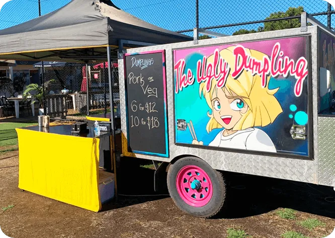 The Ugly Dumpling trailer at a market with its chalkboard menu and yellow service table